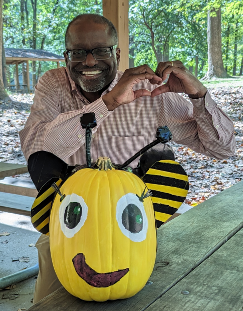 Dr. Gary H. Gibbons sitting at a picnic table with a decorative pumpkin.