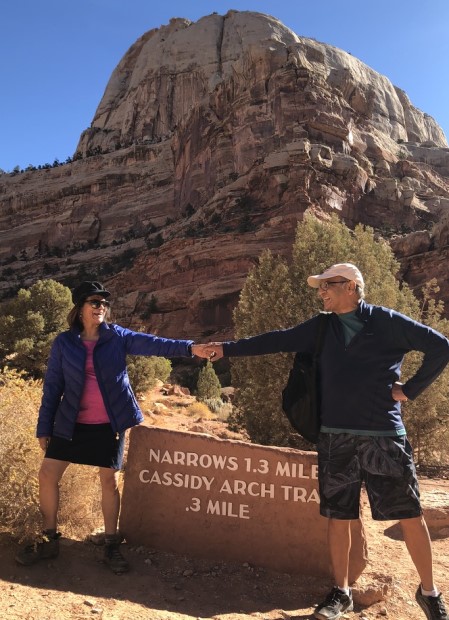 Rena and Richard D’Souza standing next to the sign for Cassidy Arch Trail at Capitol Reef National Park.
