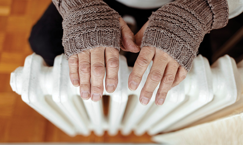 Elderly person warming their hands over a radiator